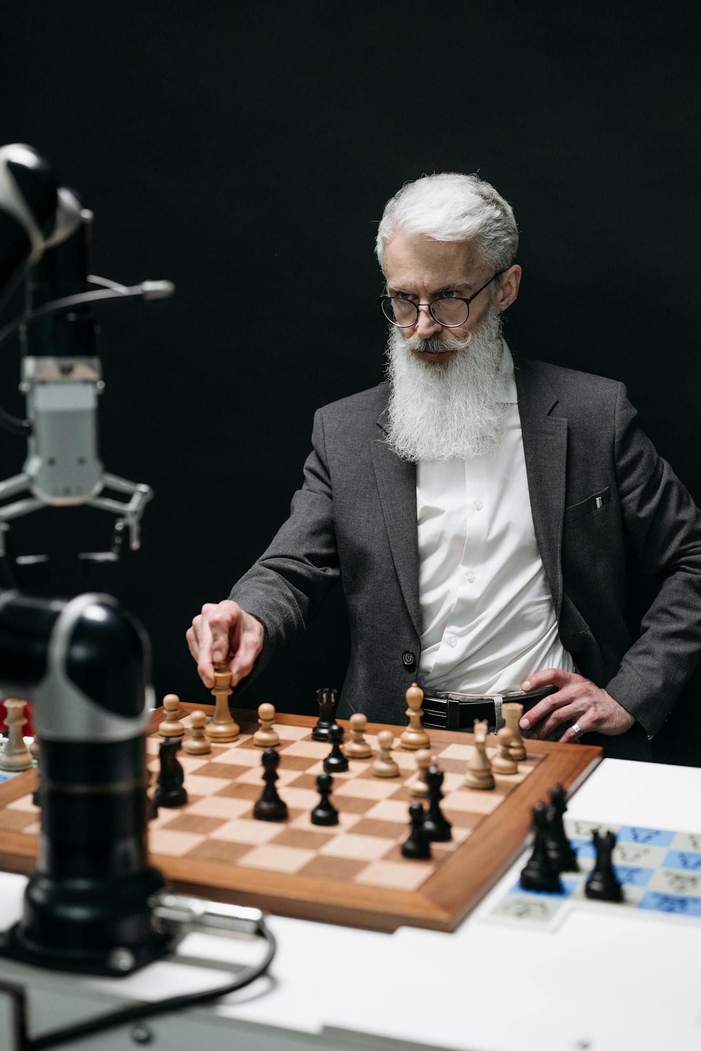 A senior scientist engages in a chess game with a robot, showcasing innovation.